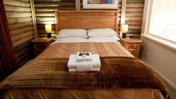 A neatly made bed with a brown blanket and white pillows, a wooden headboard, two bedside lamps, and a framed artwork above the bed.