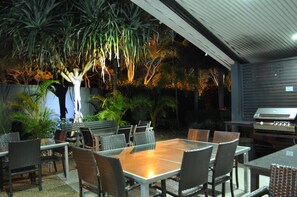 An outdoor patio with a dining table and chairs, surrounded by various plants and a grill.