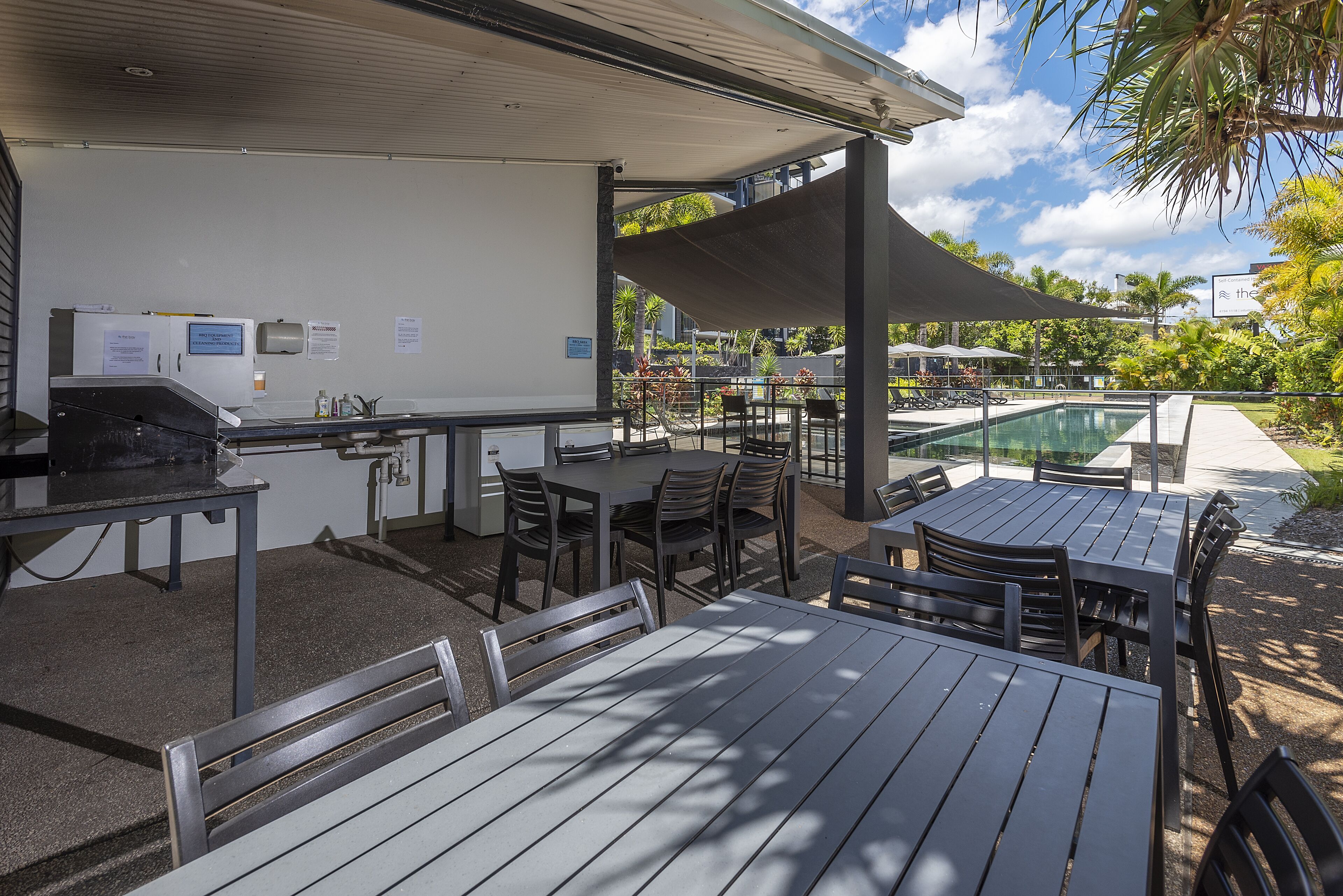 An outdoor dining area with tables and chairs, a barbecue grill, and a pool in the background.