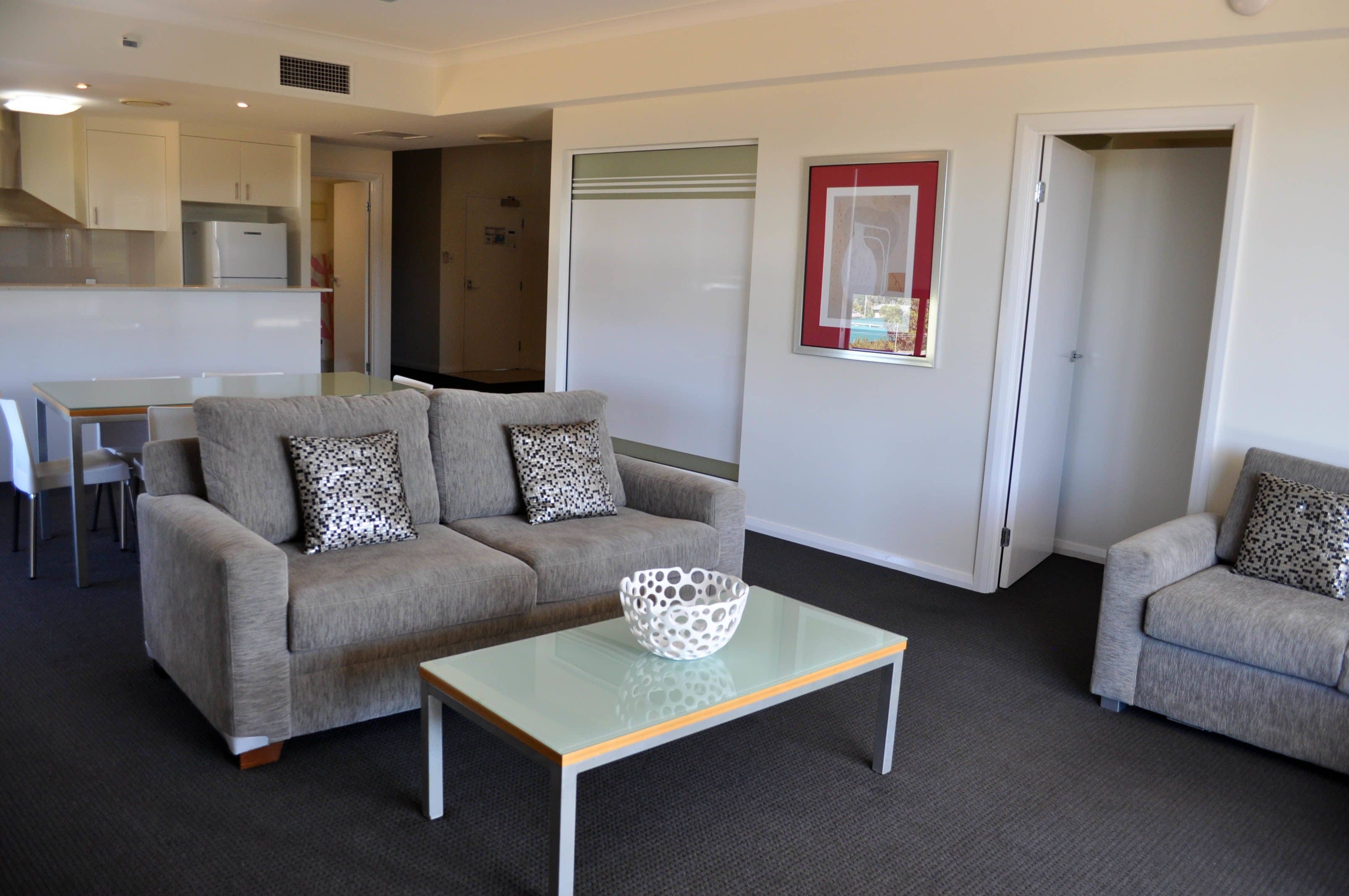 A living room with a grey sofa, a glass coffee table, and a patterned cushion.