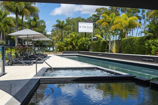 A swimming pool with lounge chairs and umbrellas, surrounded by tropical plants.