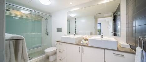 A modern bathroom with a glass shower enclosure, a toilet, and a double sink vanity with a large mirror.