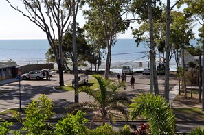 A coastal street with a view of the sea, palm trees, and parked cars.