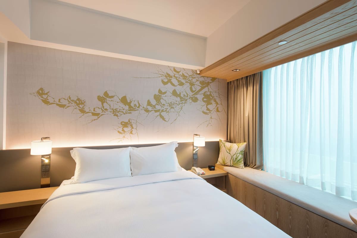 Una habitación de hotel con una cama grande, lámparas de noche, una ventana con cortinas y una pared con un mural floral.