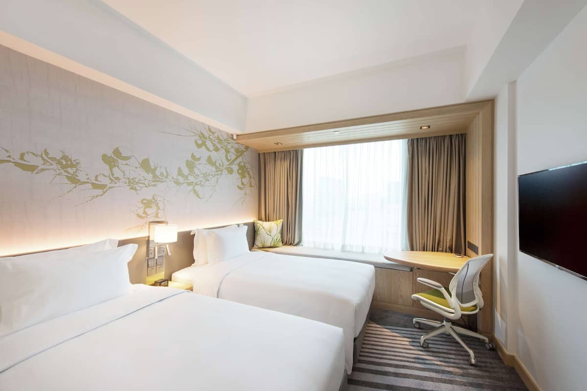 Habitación de hotel con dos camas, un escritorio, una silla, un televisor y una ventana con cortinas.