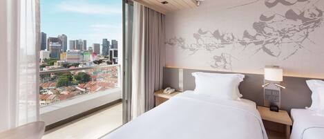 Hotelkamer met een groot raam, twee bedden, een nachtkastje met een lamp en uitzicht op de stad.