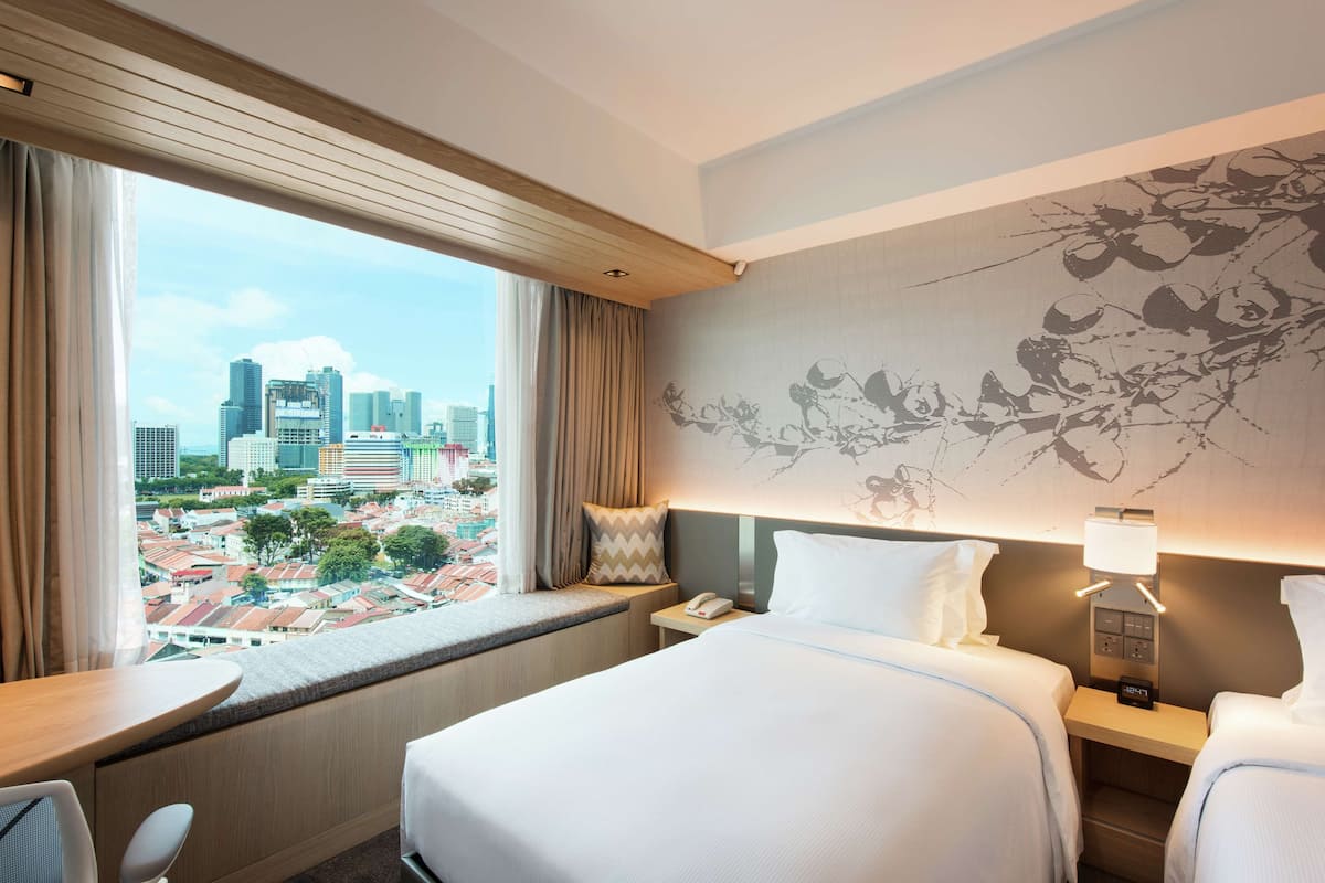 Habitación de hotel con una cama grande, un escritorio y vistas a un paisaje urbano a través de una ventana.