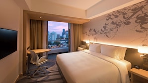 A hotel room with a large bed, a desk, a chair, a TV, and a city view. - Hilton Garden Inn Singapore Serangoon (Singapore)