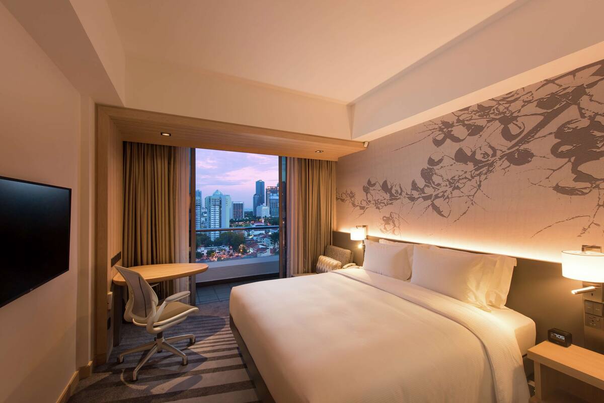 Habitación de hotel con una cama grande, un escritorio, una silla, un televisor y vistas a la ciudad.