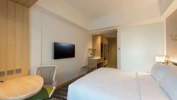 Une chambre d’hôtel avec un lit, un téléviseur fixé au mur, un bureau avec une chaise et une petite table.