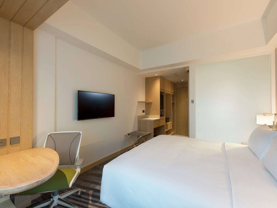 Une chambre d’hôtel avec un lit, un téléviseur fixé au mur, un bureau avec une chaise et une petite table.