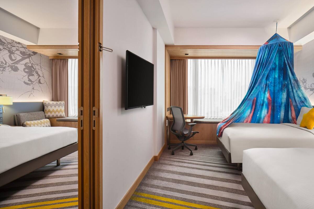Habitación de hotel con dos camas, un televisor, un escritorio con silla y una cama con dosel.