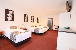 A hotel room with three beds, a desk, and a TV.