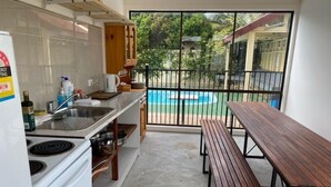 Cocina con estufa, lavamanos y armarios de madera. Se ve una piscina a través de puertas de vidrio.