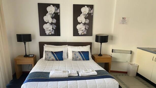 Una habitación de hotel con una cama grande, dos mesitas de noche, un escritorio y un cesto de basura.