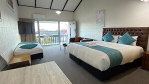 Habitación de hotel con dos camas, un sofá, una mesita y un balcón con vistas.