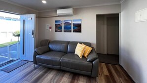 Una habitación moderna con un sofá de cuero, una puerta que da al exterior y tres cuadros en la pared.