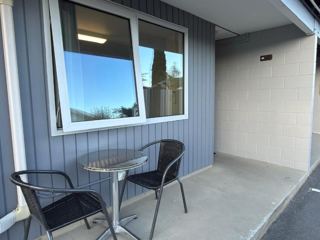A small outdoor seating area with a table and two chairs, a window, and a brick wall.