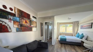 Una habitación de hotel moderna con sofá, cama con vistas, zona de comedor y un cuadro abstracto grande en la pared.