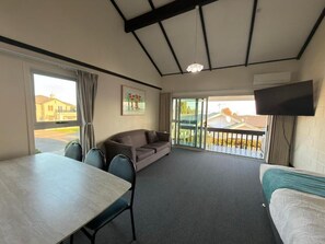 A room with a table, a sofa, a bed, a TV, and a balcony with a view of buildings. - Mountain View Motel, Taupo (Taupo)