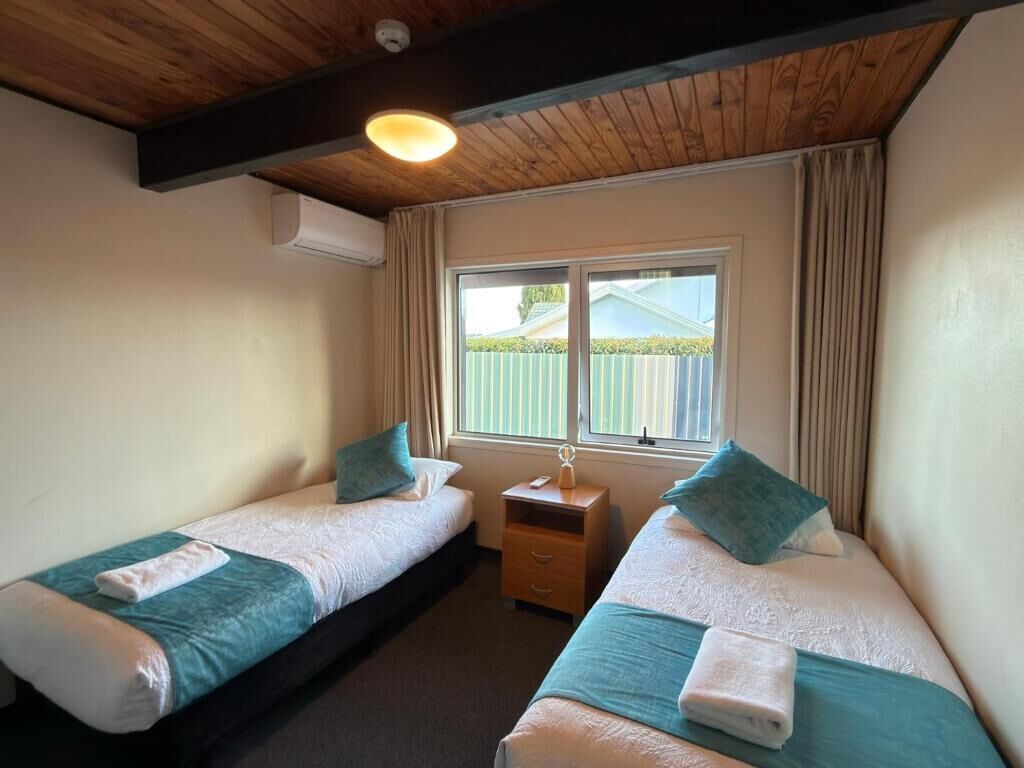 Une chambre avec deux lits, une table de chevet, une fenêtre avec des rideaux et un appareil de climatisation.