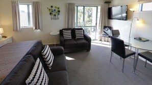 A hotel room with a bed, two sofas, a desk, and a TV. - Westport Spa Motel (Westport)