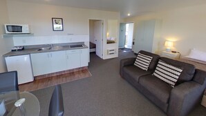 A compact living space with a kitchenette, a dining area, and a living room with a sofa and a lamp. - Westport Spa Motel (Westport)