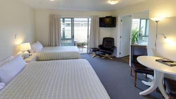 Habitación de hotel con dos camas, televisión, escritorio, silla y balcón con cortinas.