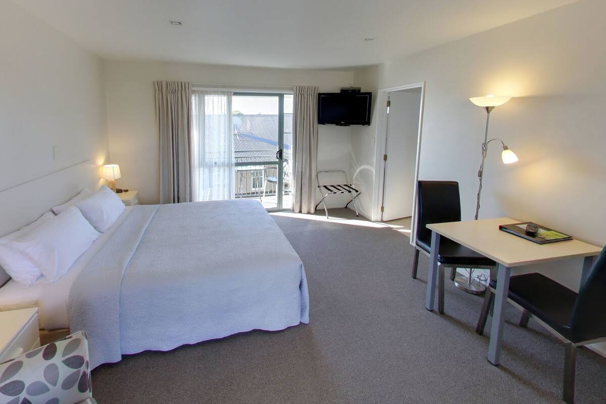 Ein Hotelzimmer mit einem großen Bett, einem Schreibtisch mit Stuhl, einem Fernseher und einem Balkon mit Stuhl und Tisch.