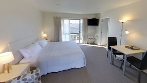 Quarto de hotel com uma cama grande, uma mesa com cadeira, televisão e varanda com cadeira e mesa.