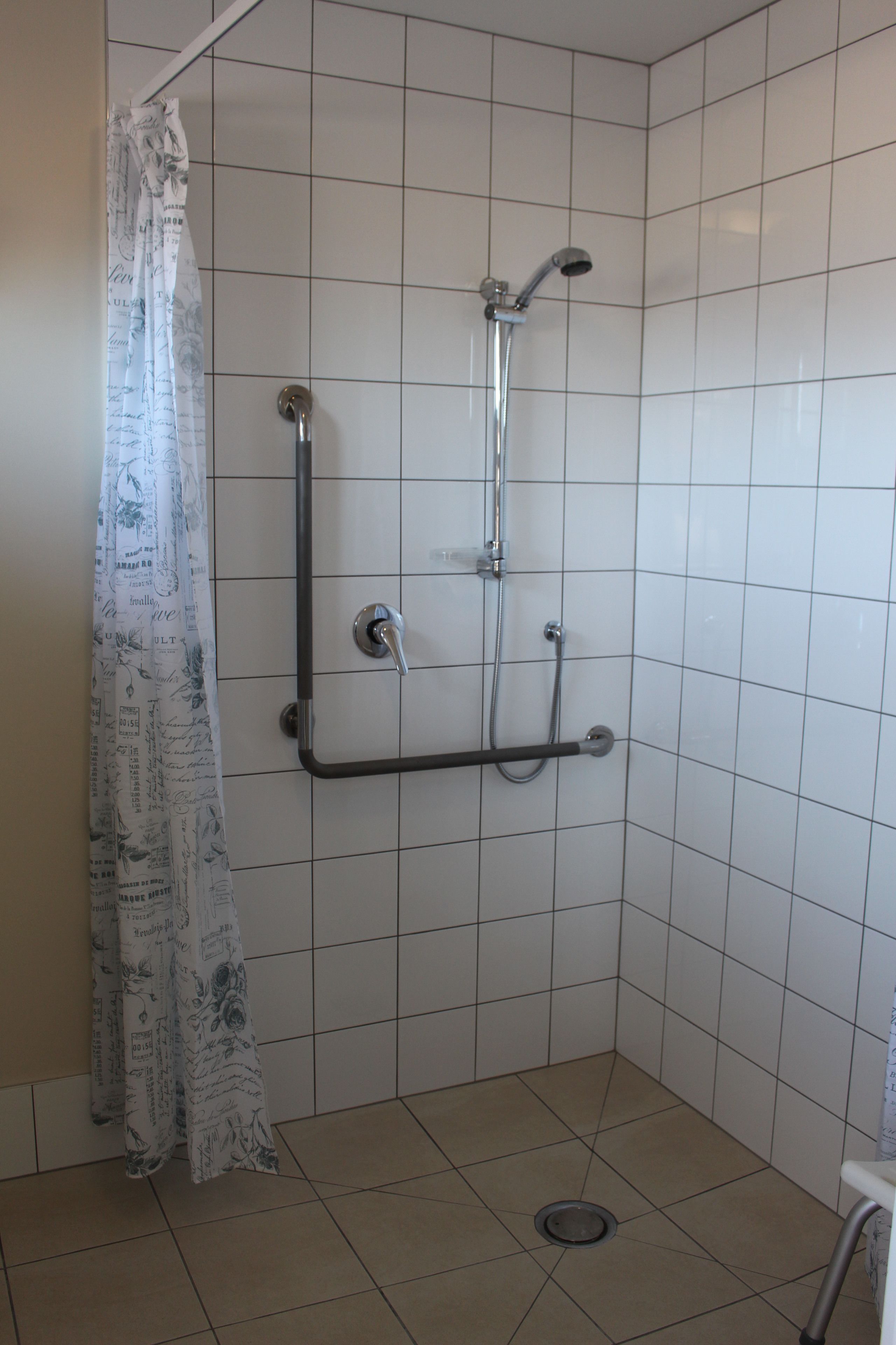 A small, tiled shower area with a showerhead, handheld shower, and a grab bar.