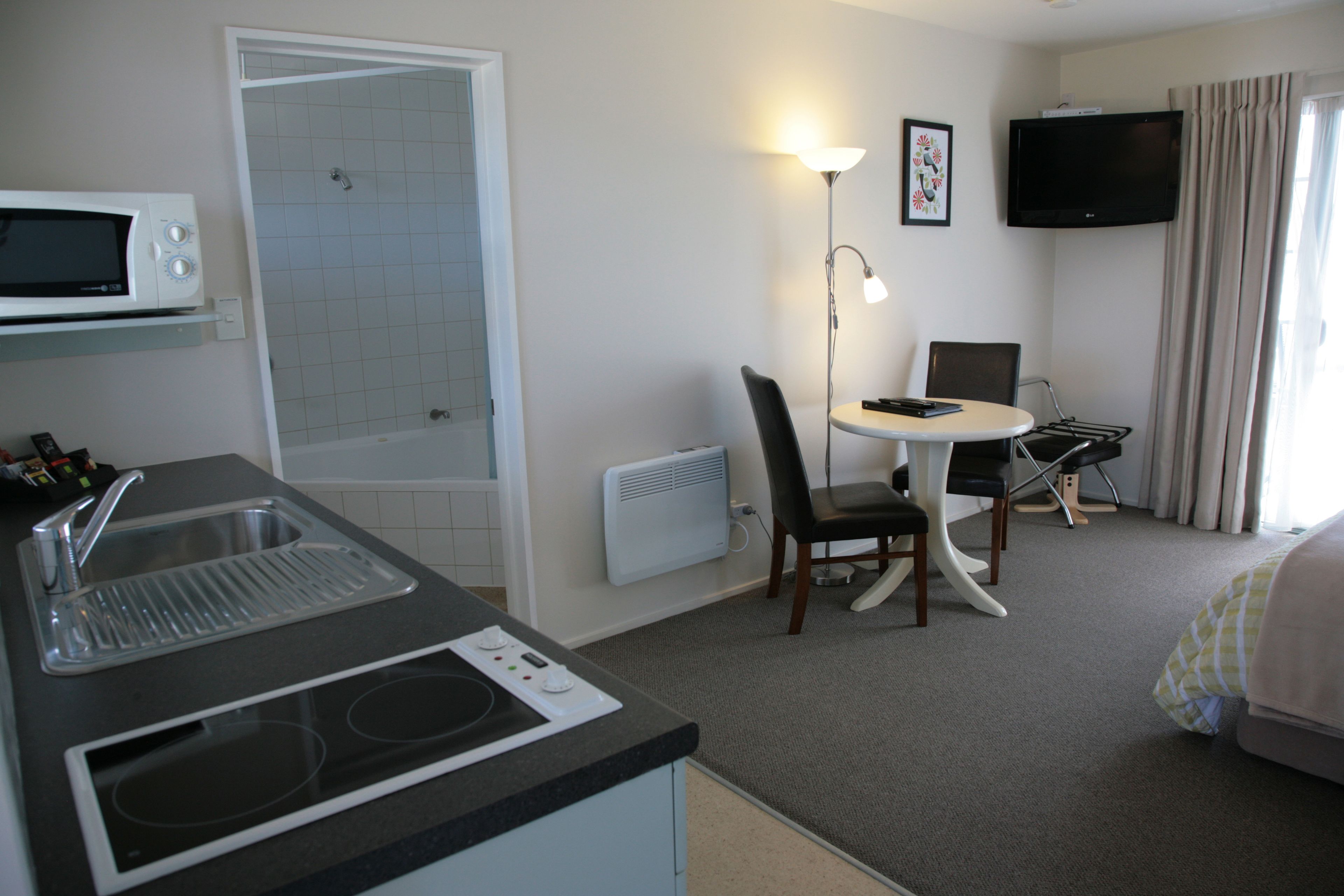 A hotel room with a kitchenette, a shower, a dining area, and a TV.