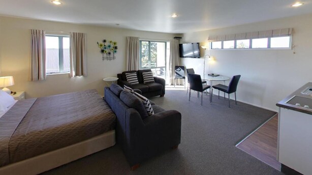 A hotel room with a bed, a sofa, a desk, and a TV. - Westport Spa Motel (Westport)