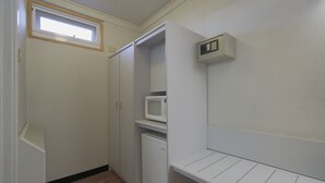 Una habitación pequeña y funcional, con microondas incorporado, un refrigerador pequeño y una ventana.