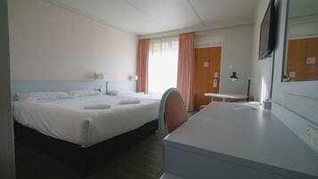 Habitación de hotel con cama, escritorio, silla, televisor y ventana con cortinas.