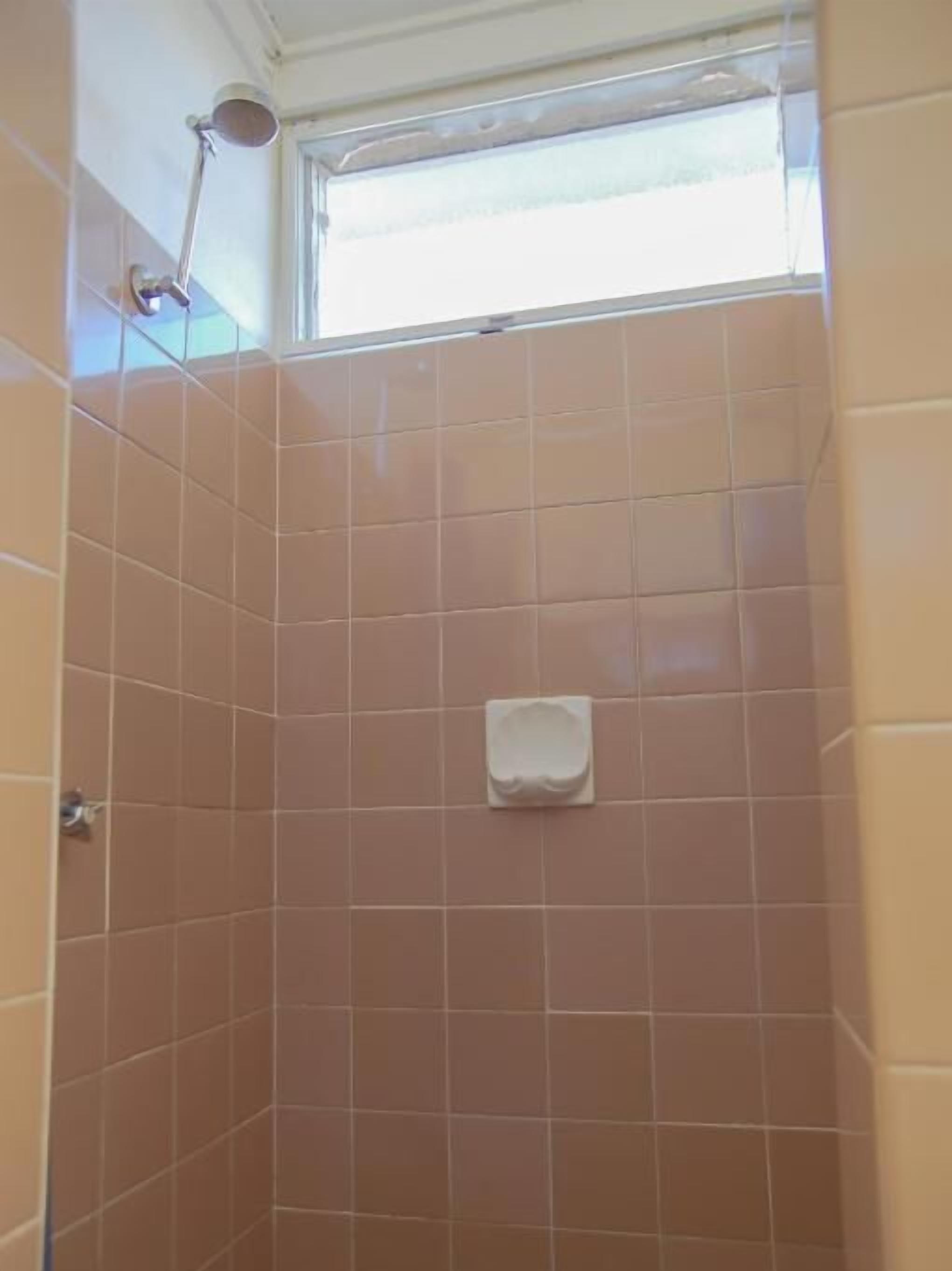 A shower with a handheld showerhead and a small towel hanging on the wall.