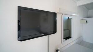 Un televisor de pantalla plana montado en la pared y un espejo en una habitación con paredes blancas y un techo con diseño empotrado.