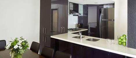 A modern kitchen with dark cabinets, a white countertop, stainless steel appliances, and a dining area with a table and chairs.