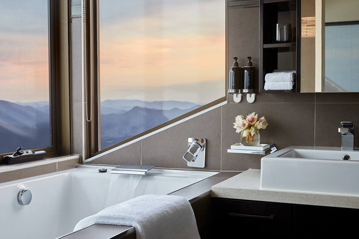 A modern bathroom with a bathtub, a sink, and a large window offering a mountain view.
