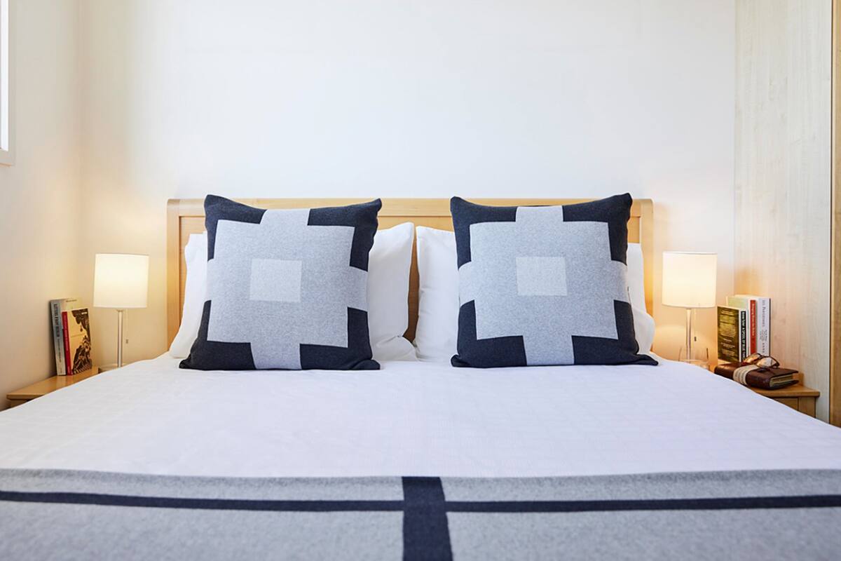 A neatly made bed with a cross-patterned bedspread, two square pillows with a geometric design, and two bedside lamps on wooden nightstands.