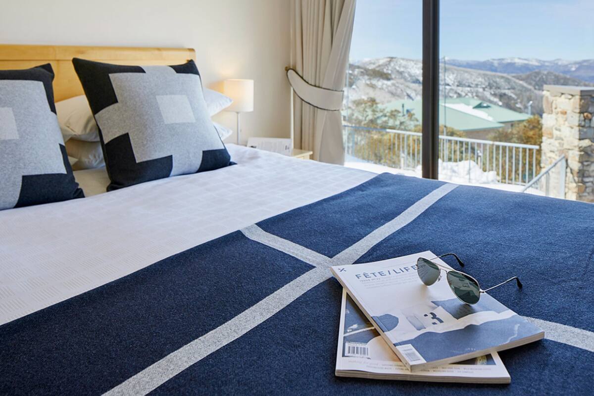 A hotel room with a large bed, a view of the mountains, and a balcony with a railing.