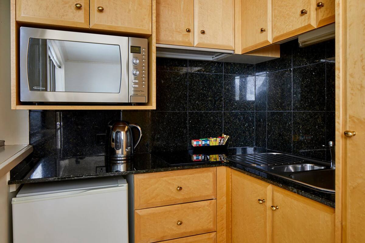A compact kitchen with a microwave, kettle, and a small refrigerator.