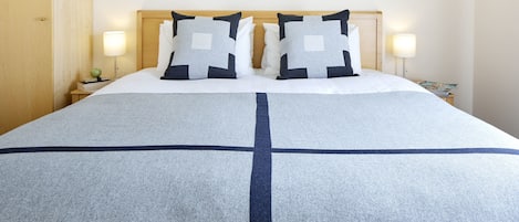 A neatly made bed with a cross-patterned bedspread, two pillows with a geometric design, and two bedside lamps on wooden nightstands.