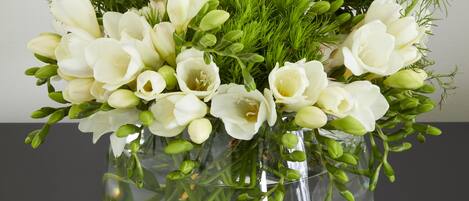 A clear glass vase with a bouquet of white flowers and green foliage.