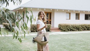A woman standing in front of a white building with a tiled roof, a wooden door, and a small porch with steps leading up to it. - Yallingup Villas (Yallingup)