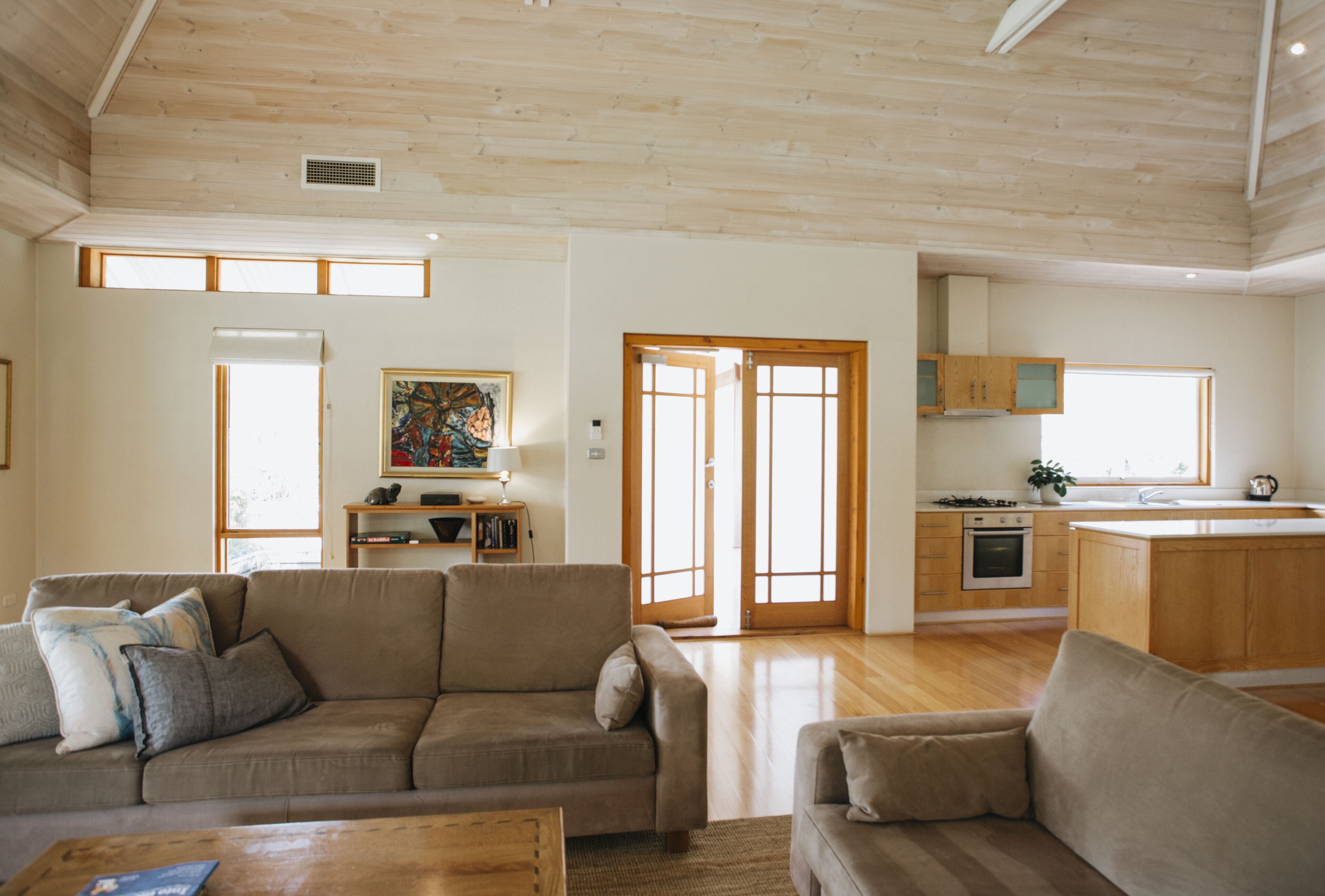 A spacious living area with a wooden ceiling, a sofa, a coffee table, and a kitchen in the background.