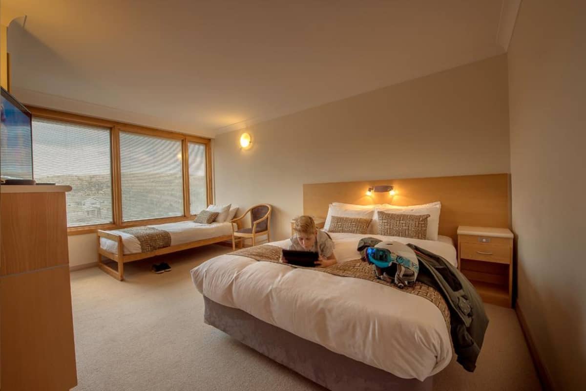 Een slaapkamer met een groot bed, een nachtkastje, een stoel en een raam met jaloezieën.
