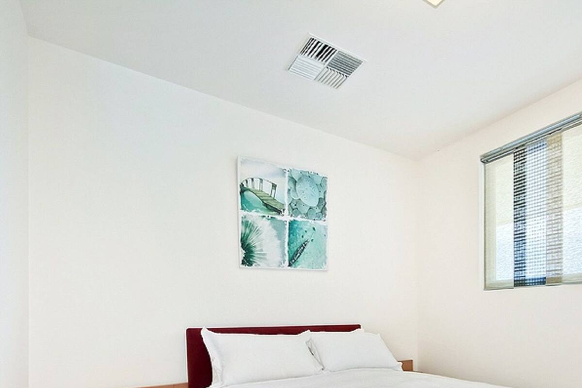 Quarto com cama, mesa de cabeceira, aparador e janela com persianas.