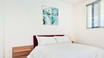 A bedroom with a bed, a nightstand, a drawer unit, and a window with blinds.