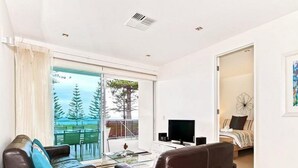 Uma sala de estar moderna com uma grande porta de vidro deslizante que dá para uma varanda, uma televisão de tela plana e uma área de estar confortável.